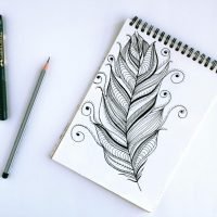 Artistic feather sketch with pen and pencil on sketchpad, showcasing intricate details.